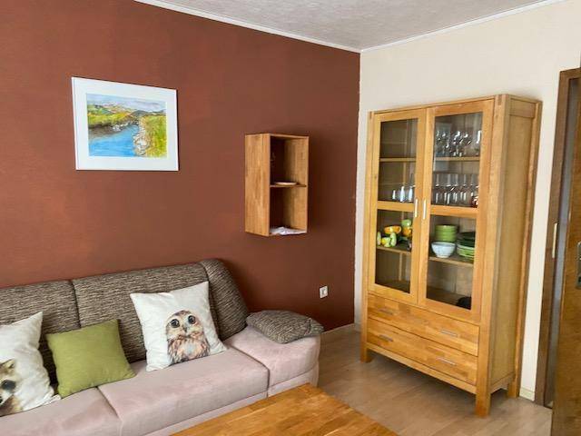 Gemütliches Wohnzimmer mit beigem Sofa, Holzschrank und einer warmen braunen Akzentwand.