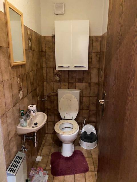 Kleines Gäste-WC mit braunen Fliesen, Toilette und Handwaschbecken.