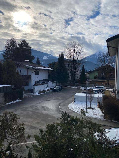 Winterliche Berglandschaft mit verschneiten Häusern und Straße unter bewölktem Himmel.