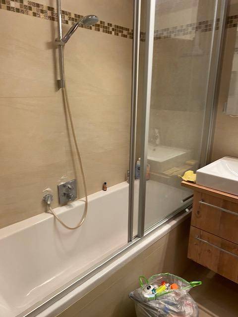 Badezimmer mit Badewanne und Duschfunktion, umgeben von hellen Fliesen.