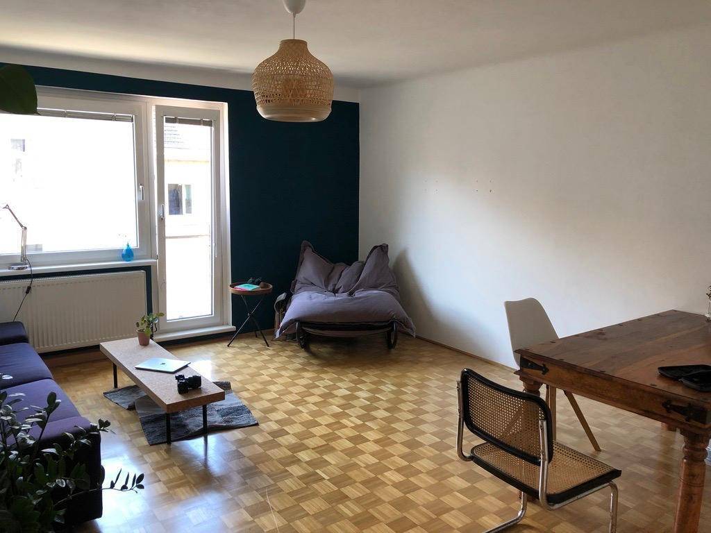 Geräumiger Wohn-Essbereich mit Parkettboden, dunkler Akzentwand und Zugang zum Balkon.