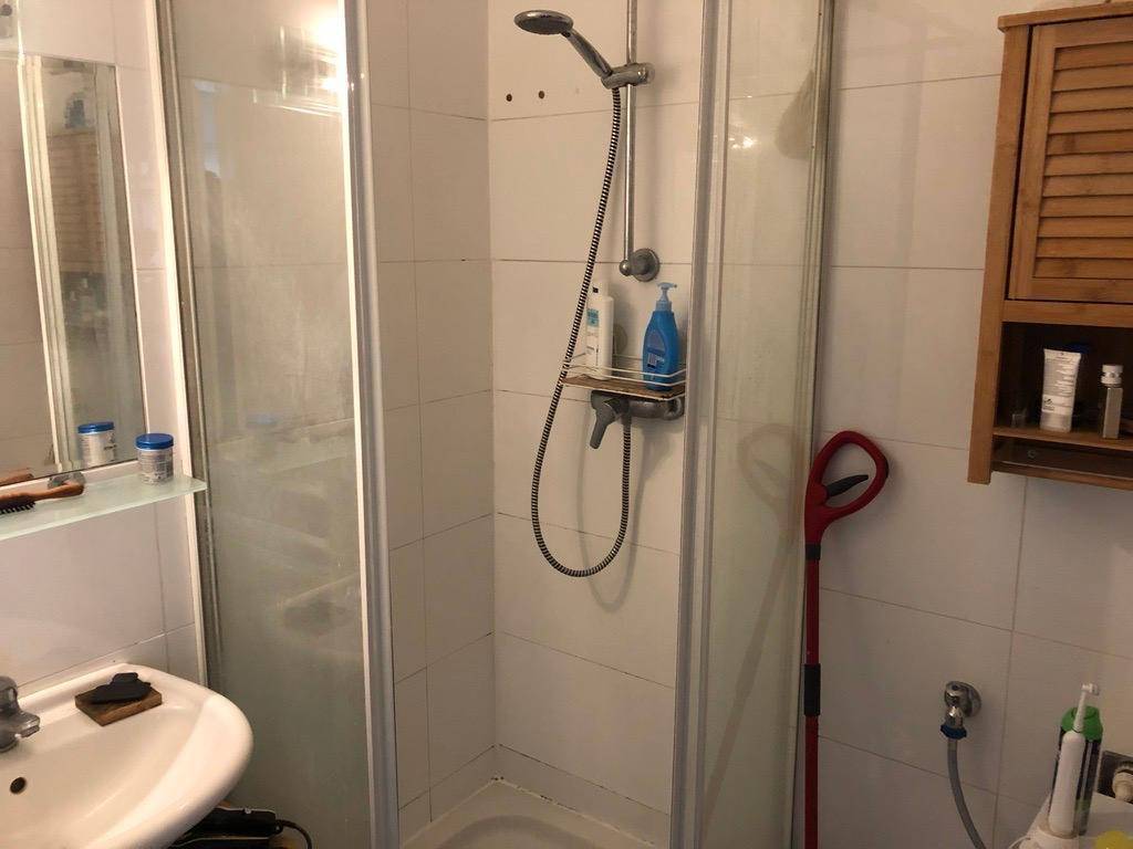 Funktionales Badezimmer mit Duschkabine, Waschbecken und einem kleinen Holzschrank.