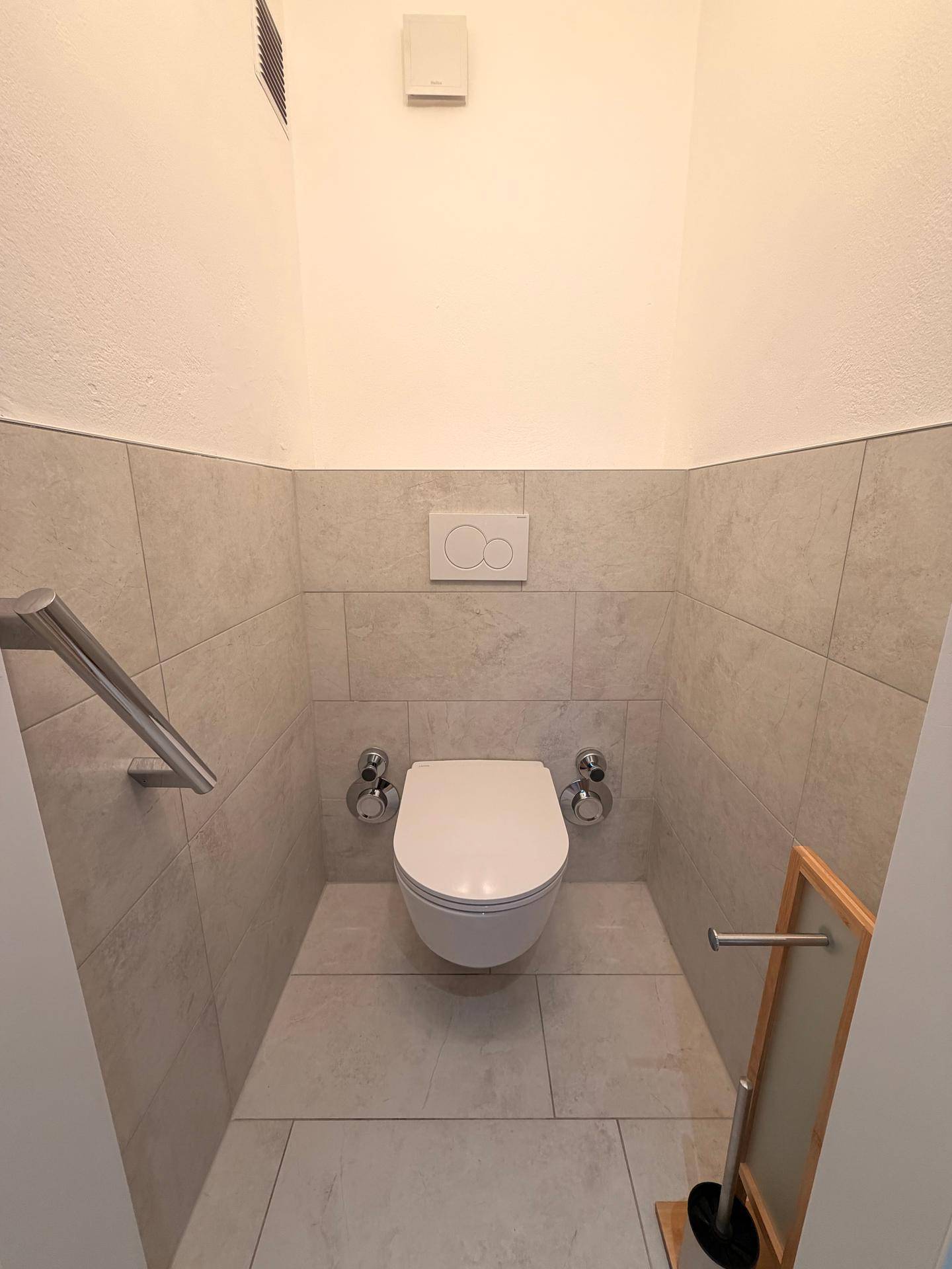 Modernes Gäste-WC mit wandhängender Toilette und Haltegriffen.