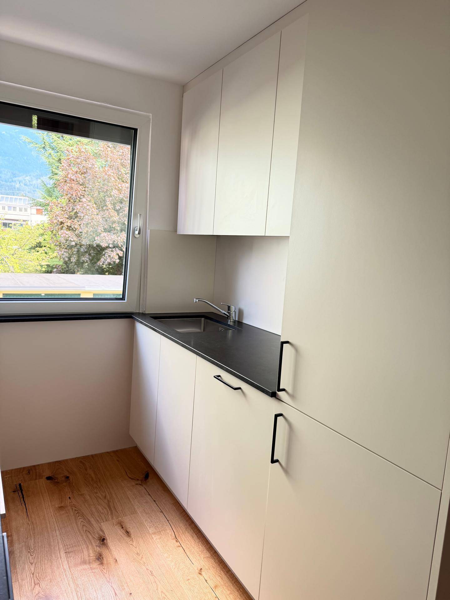 Küchenzeile mit Spülbecken, weißen Schränken und Fenster mit Blick ins Grüne.