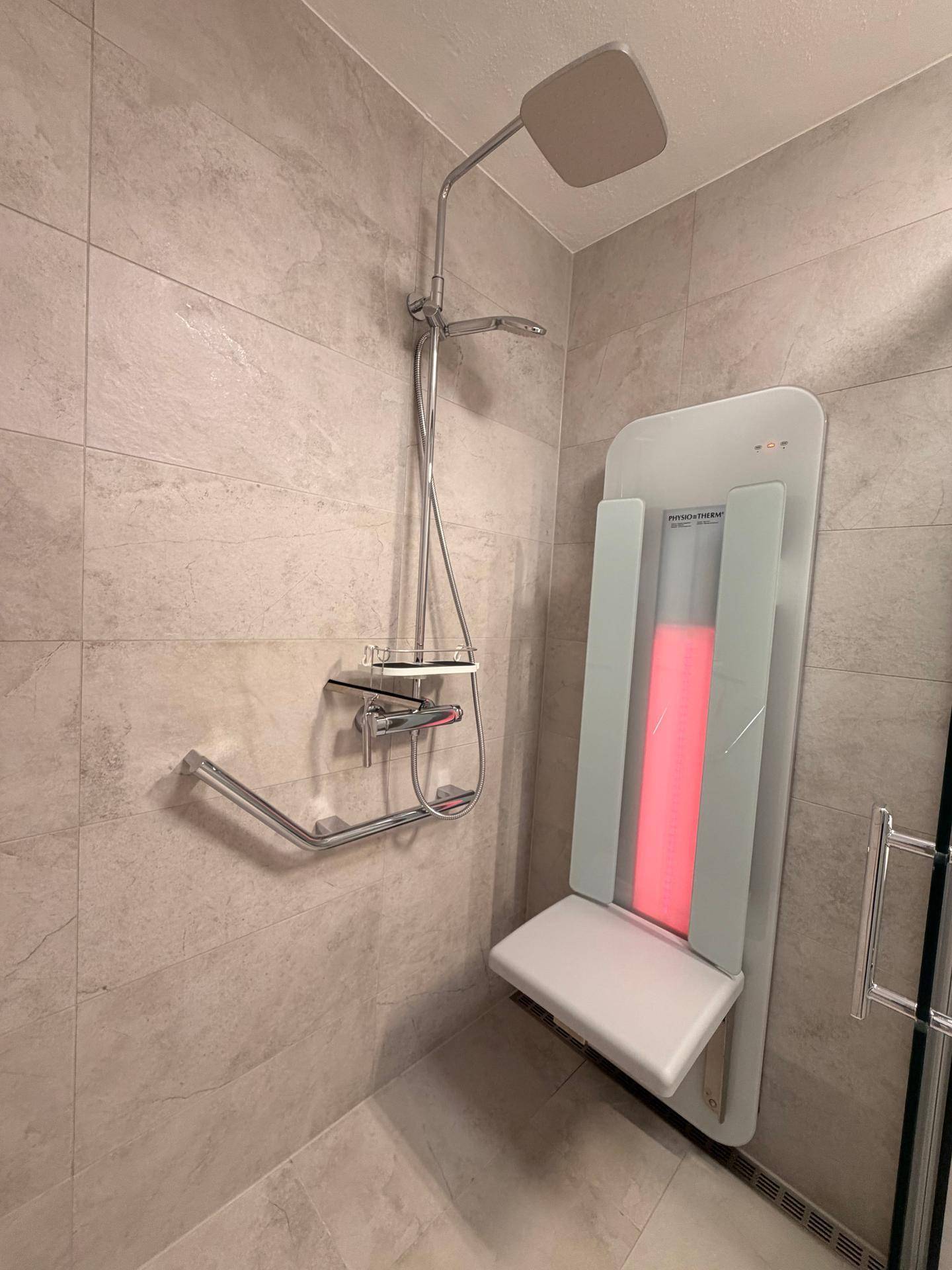 Barrierefreie Dusche mit Haltegriffen und klappbarem Duschsitz in modern gefliestem Bad.
