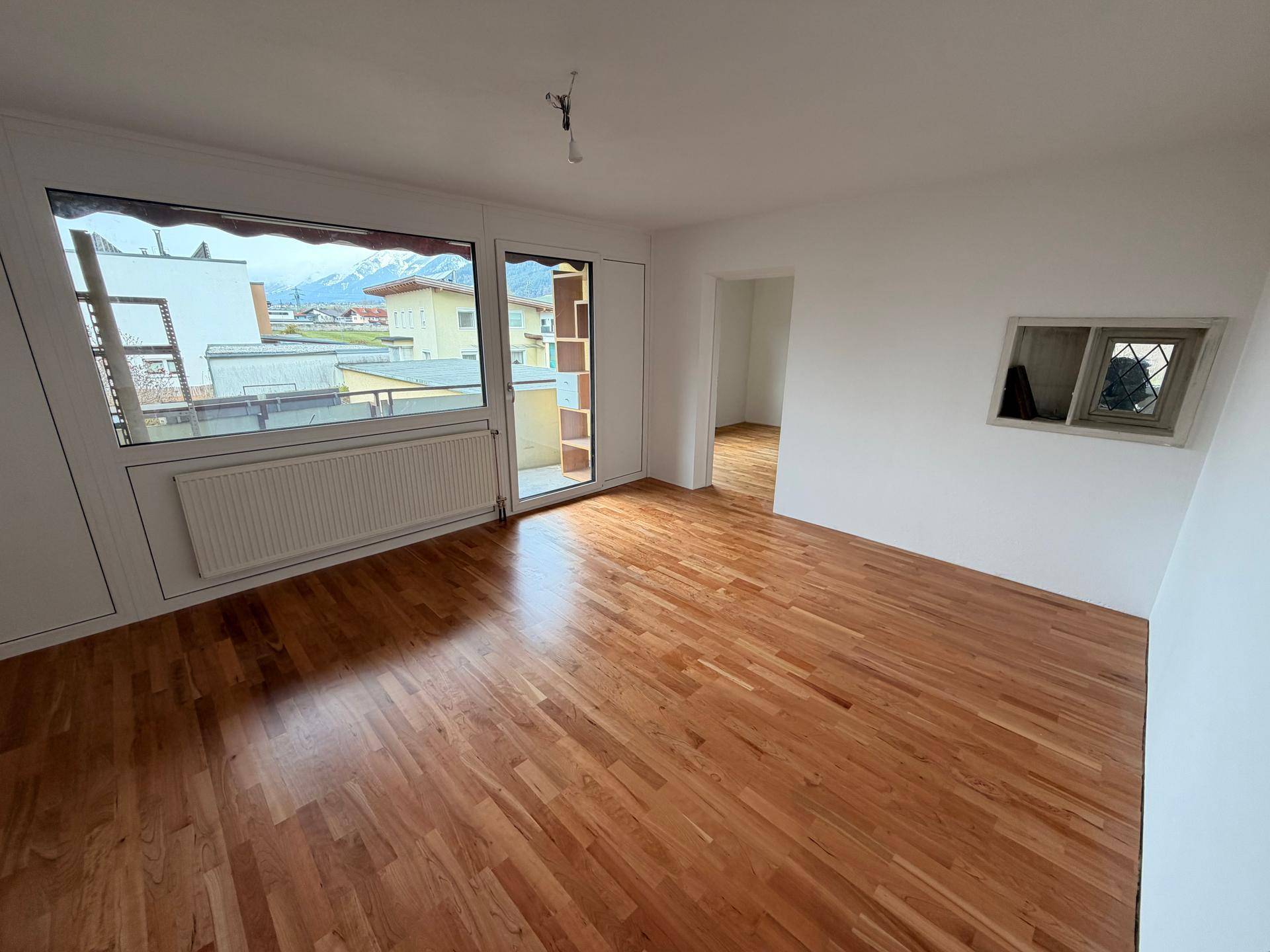 Helles Wohnzimmer mit Holzboden, Zugang zur Loggia und Bergblick.