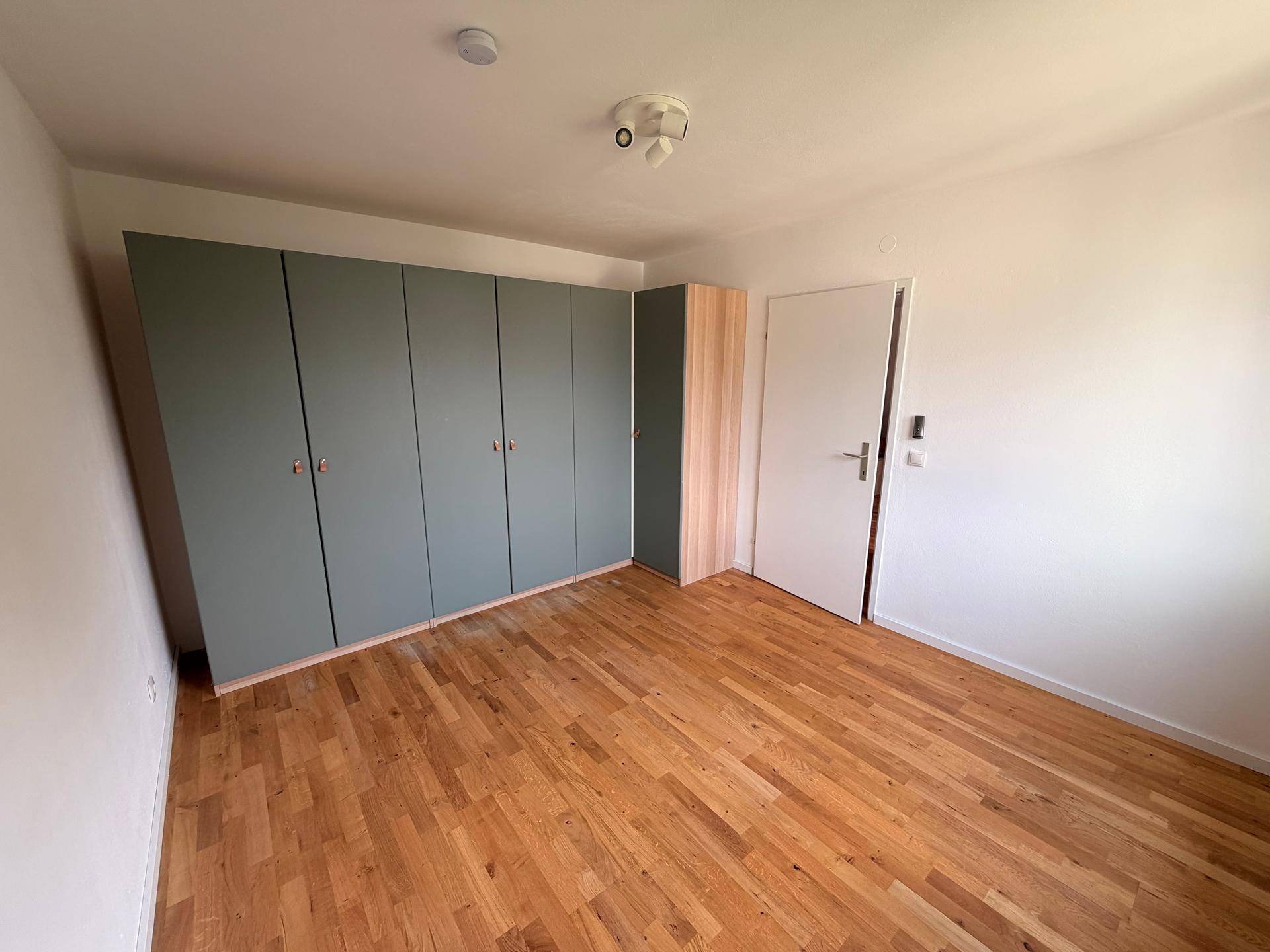 Schlafzimmer mit hellem Holzfußboden und großem, modernem Einbauschrank.