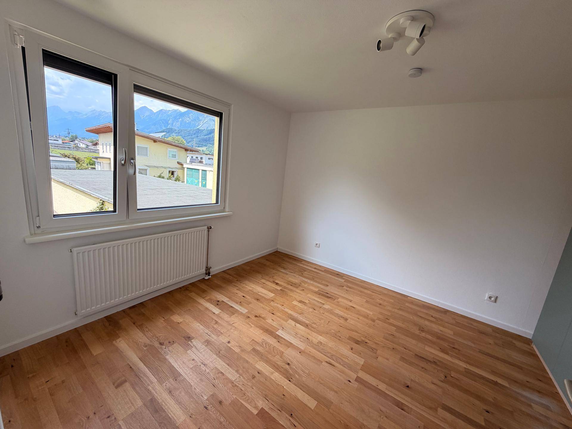 Schlafzimmer mit Holzboden, Heizkörper unter dem Fenster und Bergblick.