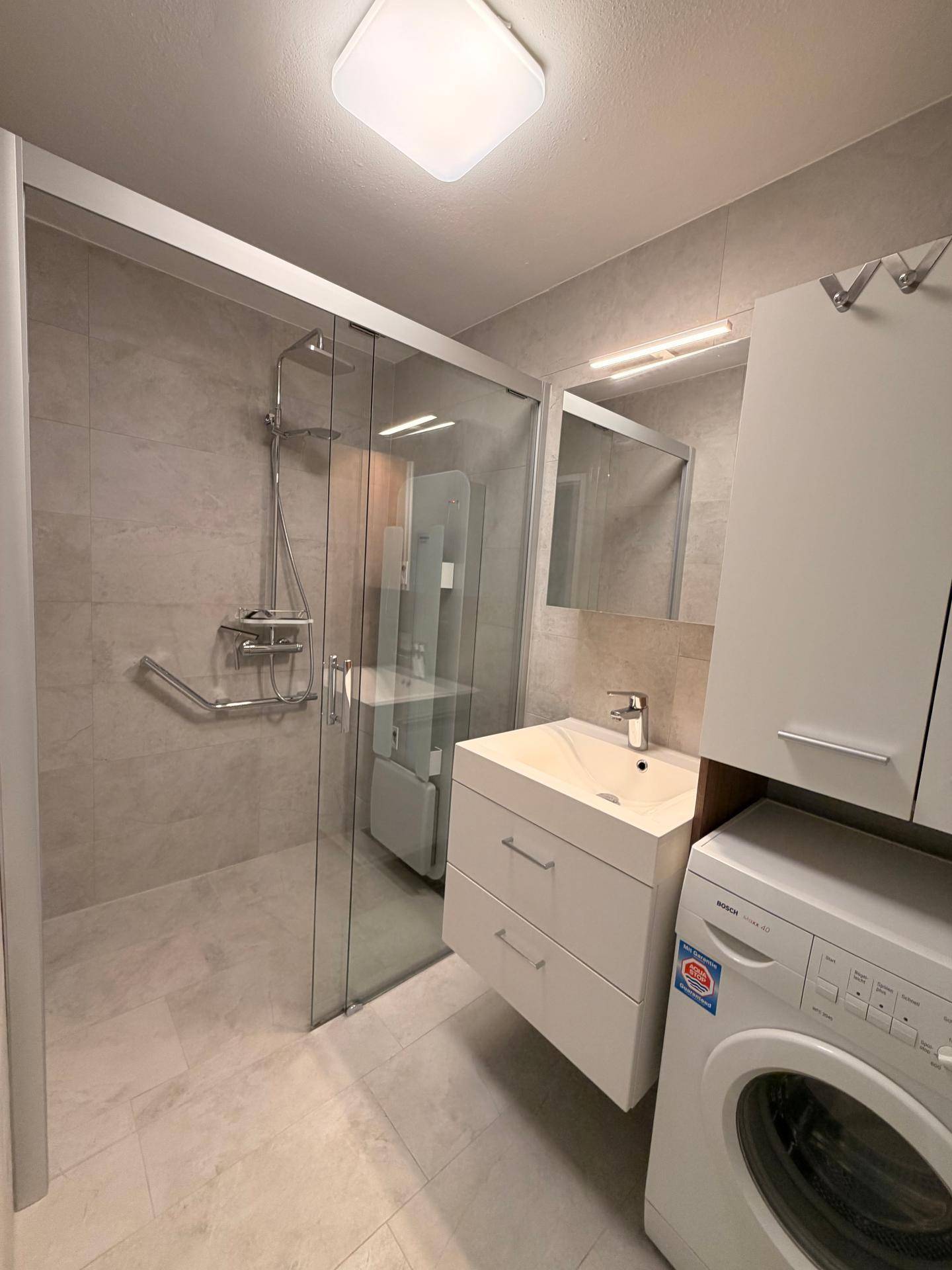 Modernes Badezimmer mit Duschkabine, Waschbecken und integrierter Waschmaschine.