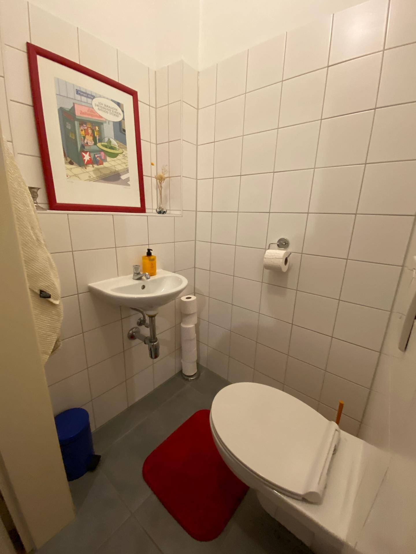 Kleines Gäste-WC mit weißen Fliesen, Toilette und Waschbecken.