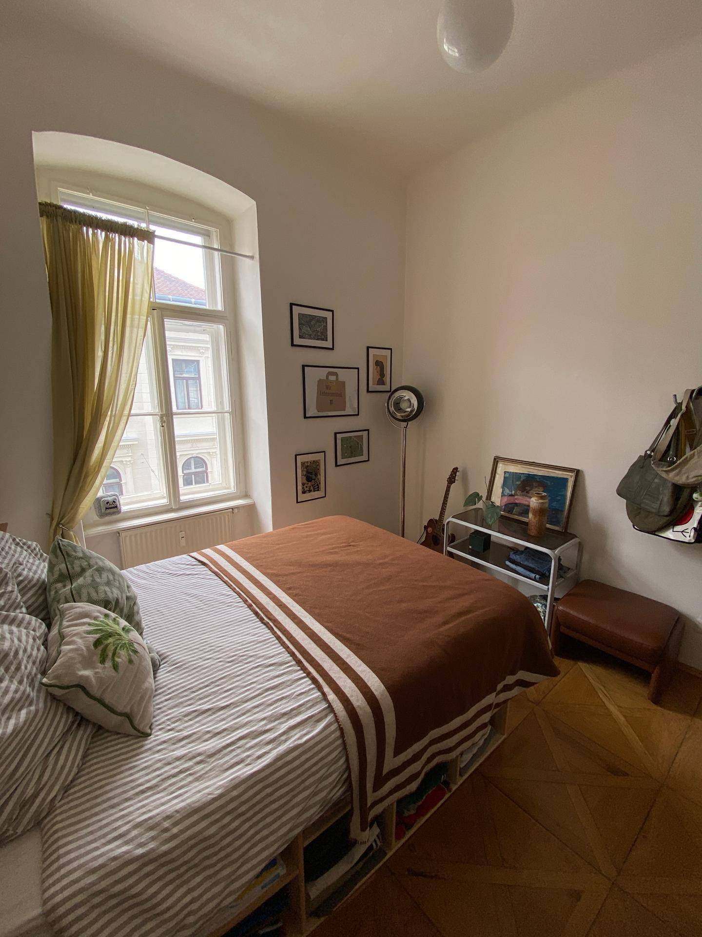 Gemütliches Schlafzimmer mit Bett, Fenster und Blick auf die umliegenden Gebäude.