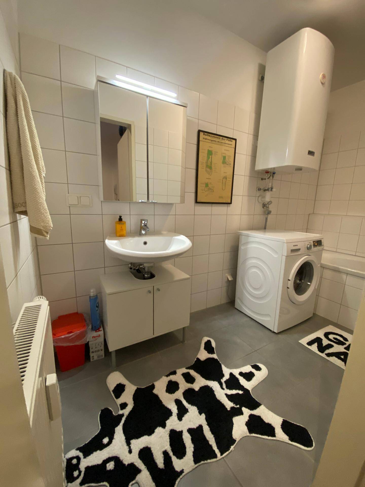 Badezimmer mit Waschbecken, Waschmaschine und einem dekorativen Teppich.