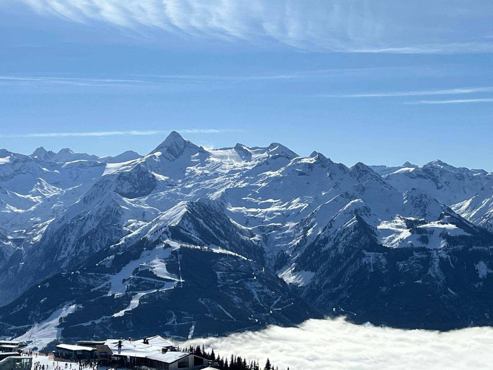 Atemberaubender Panoramablick auf schneebedeckte Alpengipfel und Skipisten über einer Wolkendecke.