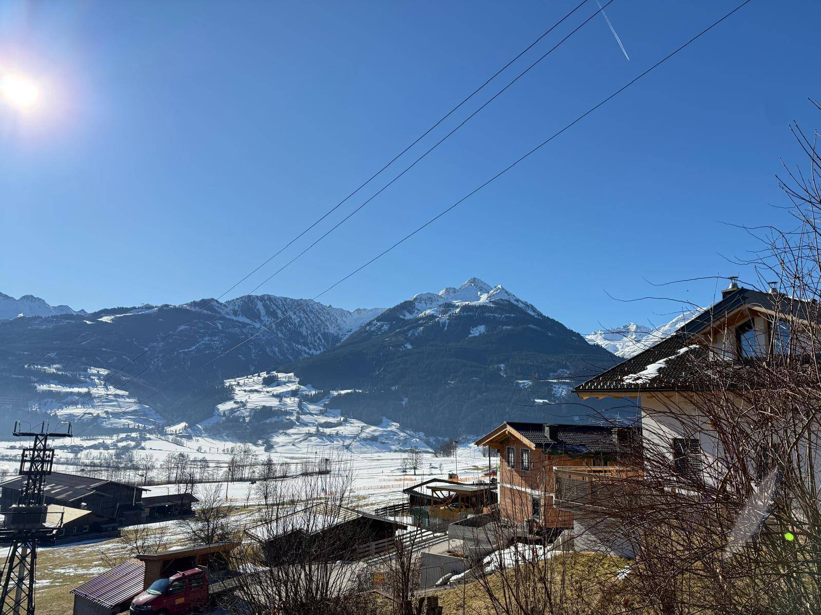 Winterlandschaft mit schneebedeckten Bergen und Häusern unter strahlend blauem Himmel.