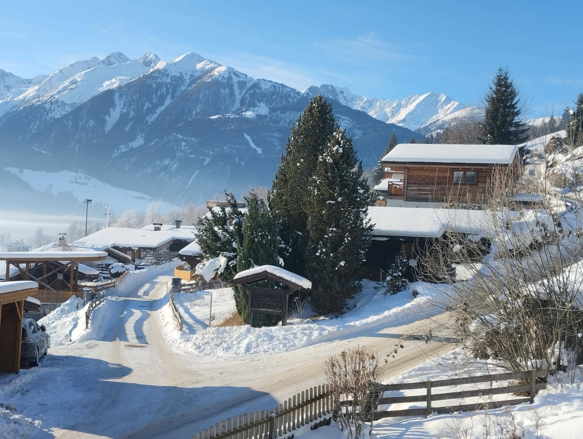 Verschneite Berglandschaft mit traditionellen Holzhäusern und Tannenbäumen an einem sonnigen Tag.