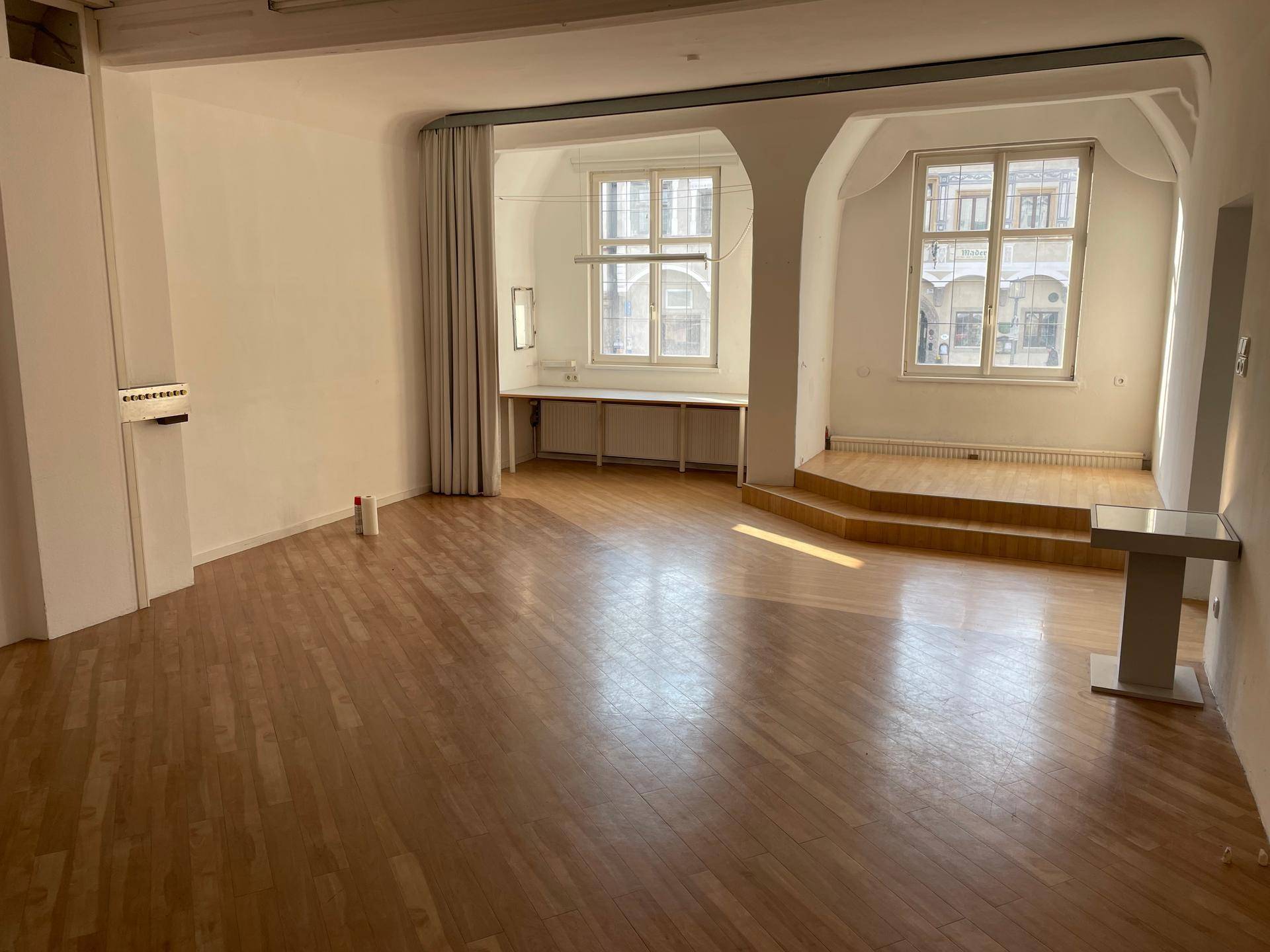 Geräumiger offener Innenraum mit Holzboden, hohen Decken und großen Fenstern, die viel Tageslicht hereinlassen.