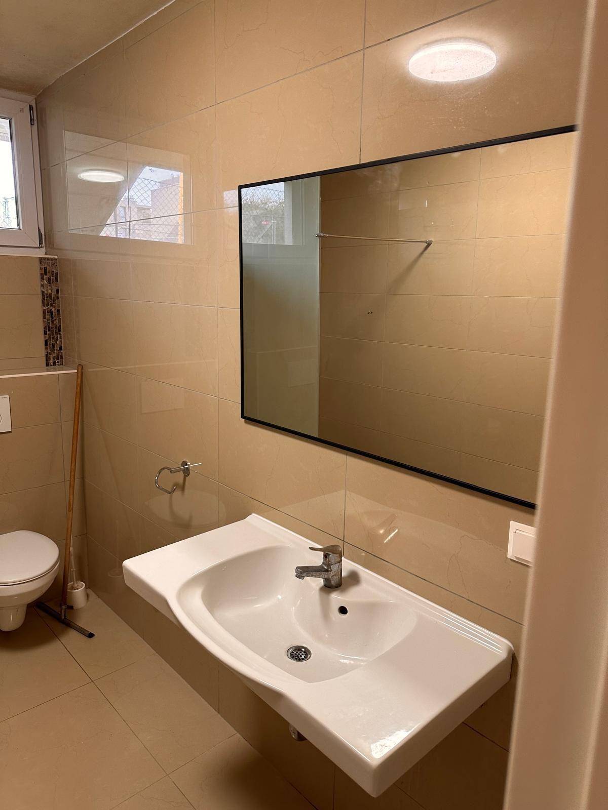 Badezimmer mit modernem Waschbecken, großem Spiegel und Fenster für natürliche Belichtung.