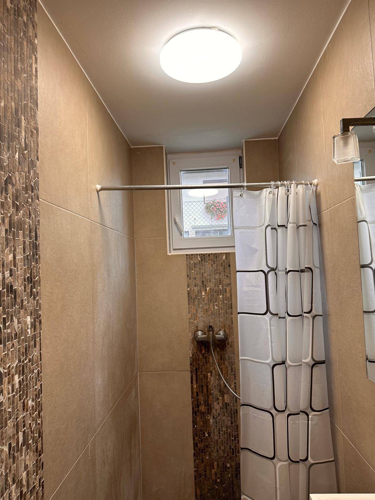 Modern gefliestes Badezimmer mit Duschbereich und einem kleinen Fenster.