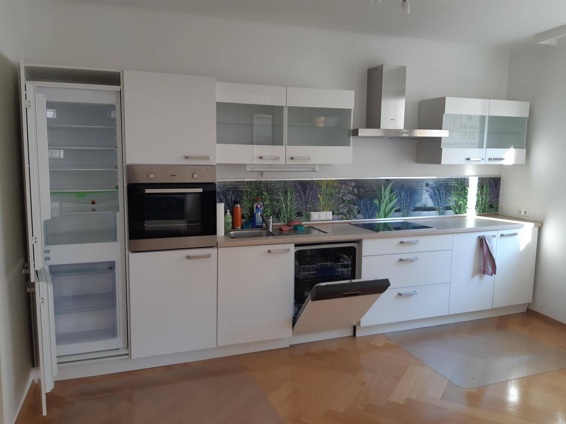 Moderne Einbauküche in Weiß mit integrierten Geräten und farbiger Rückwand.