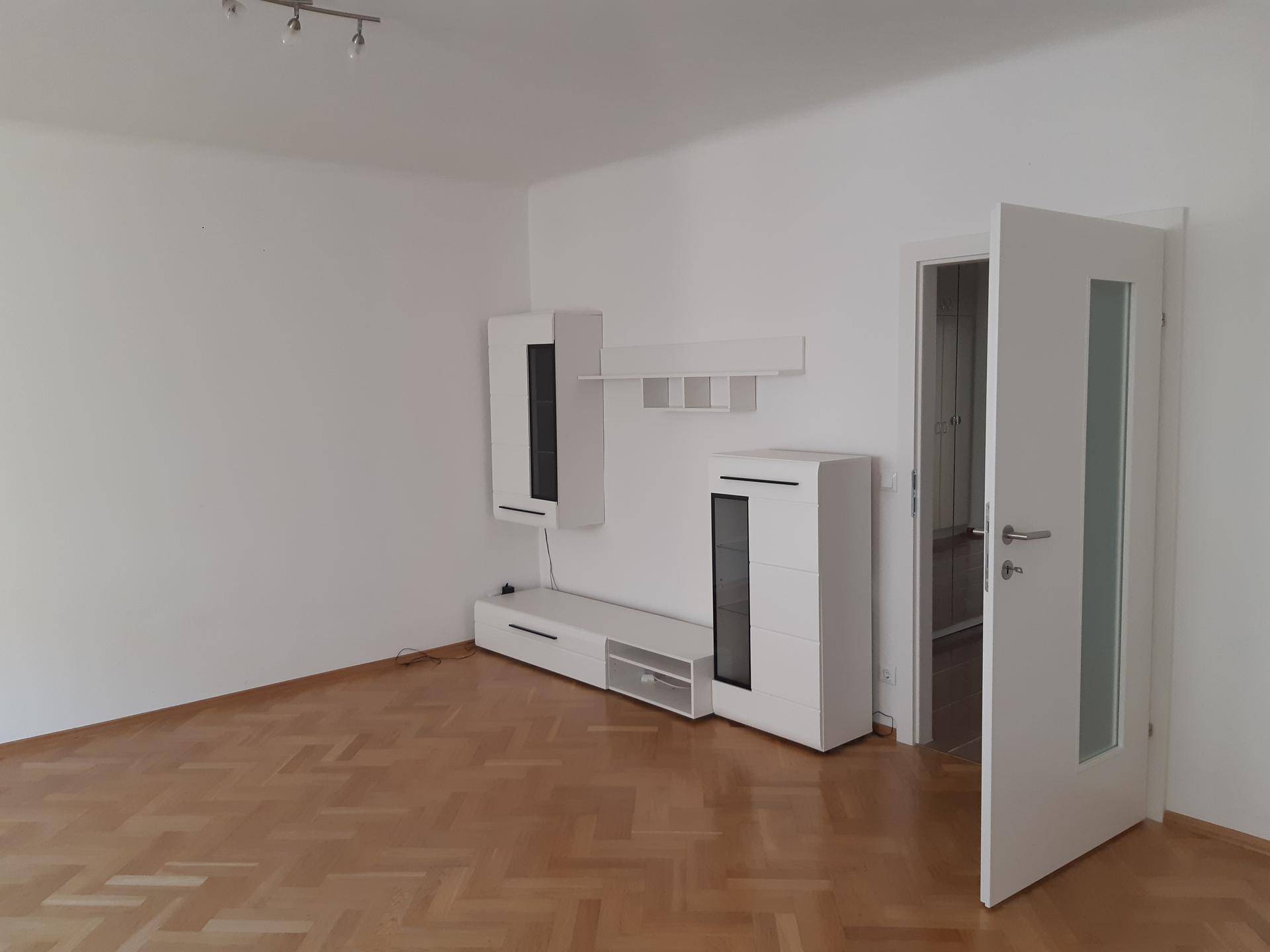 Geräumiges Wohnzimmer mit Parkettboden und moderner weißer Wohnwand.
