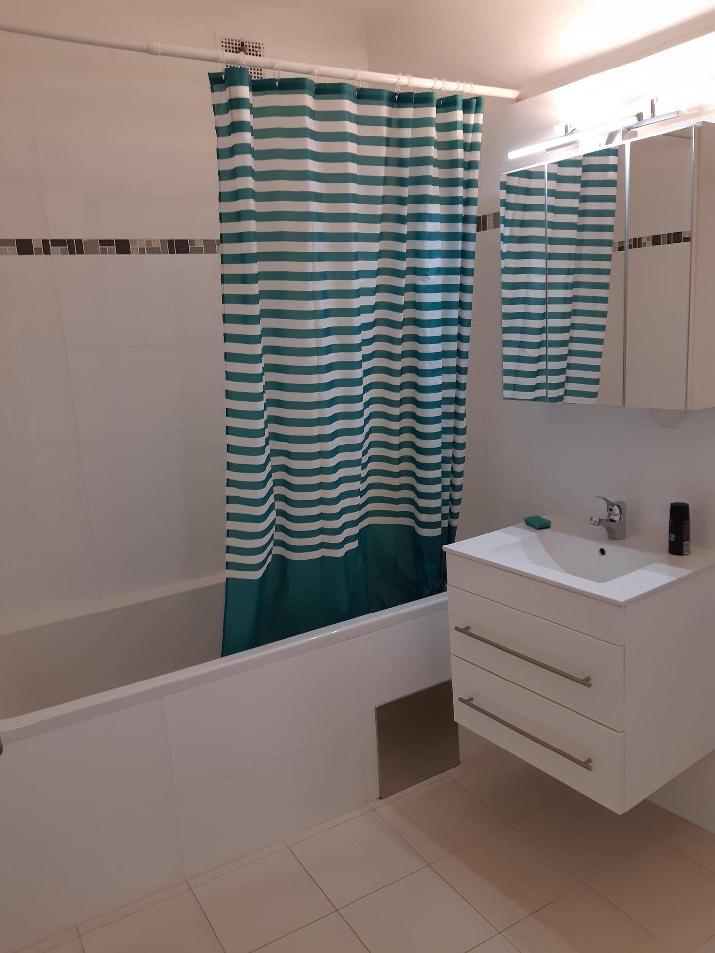 Badezimmer mit Badewanne, Duschvorhang, Waschbecken und Spiegelschrank.