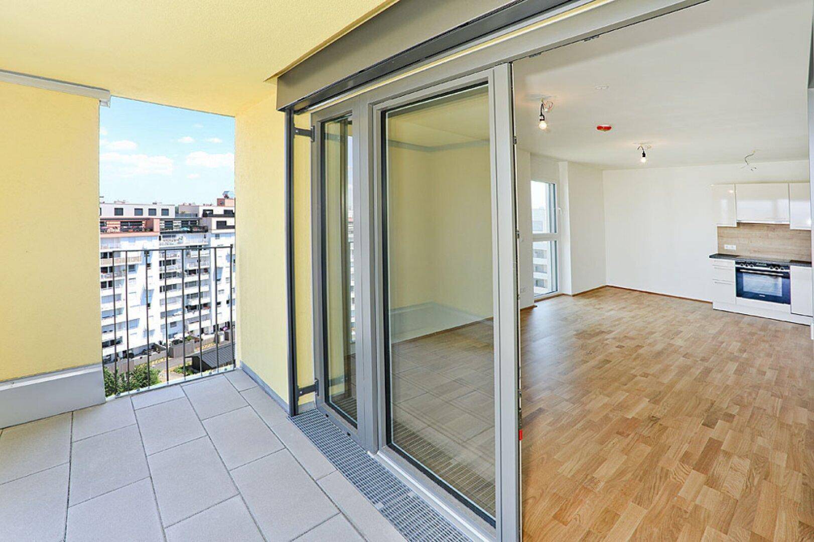 Heller Wohnbereich mit integrierter Küche und Zugang zum Balkon mit Stadtblick.