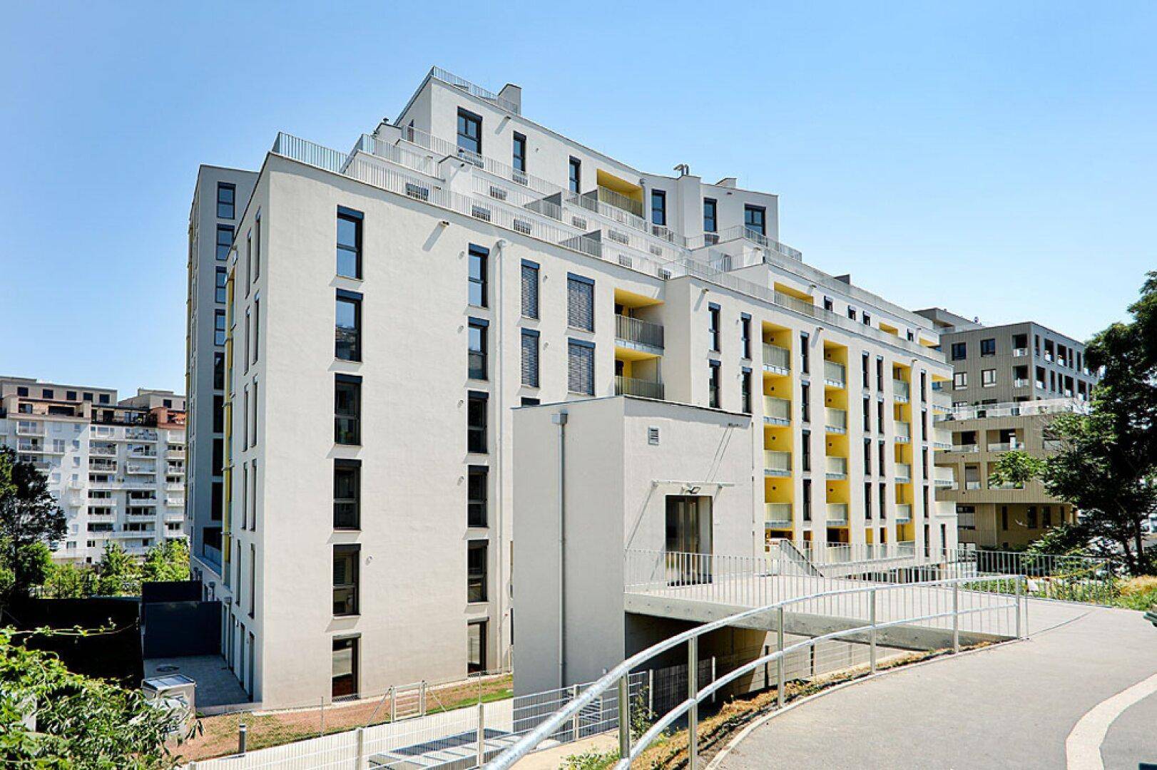 Modernes Wohngebäude mit gestufter Architektur und gelben Balkonakzenten unter blauem Himmel.