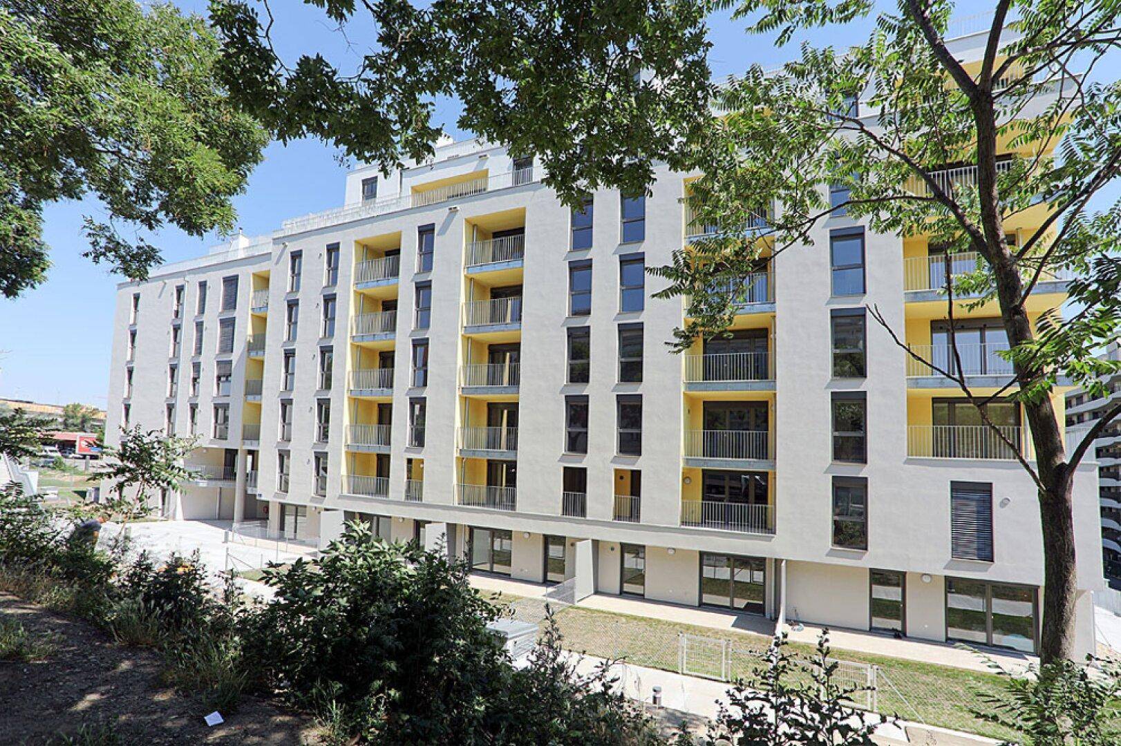 Ansicht eines modernen Wohnkomplexes mit vielen Balkonen und grüner Umgebung.