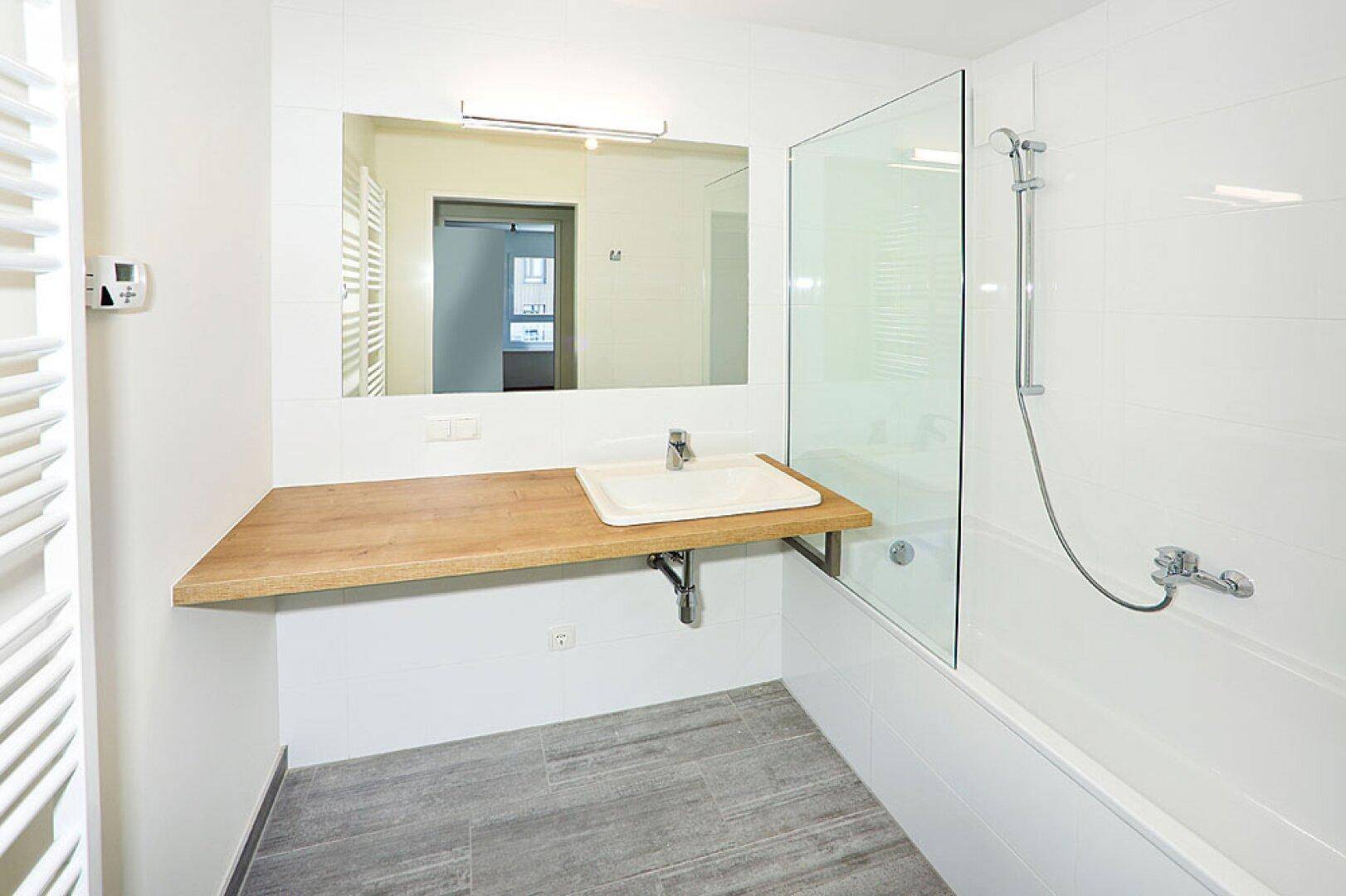 Modernes Badezimmer mit Holztischplatte, Waschbecken und Badewanne mit Duschabtrennung.
