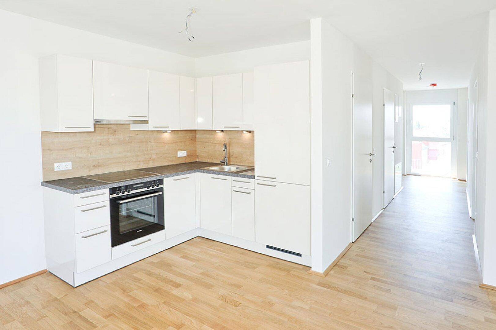 Moderne Einbauküche mit weißen Hochglanzfronten und integrierten Geräten in offenem Bereich.