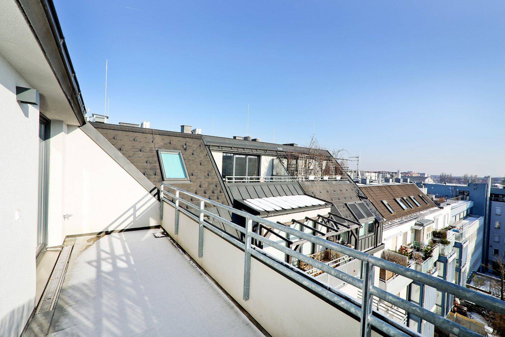 Weitläufige Dachterrasse mit Metallgeländer und Panoramablick über die Dächer der Stadt.