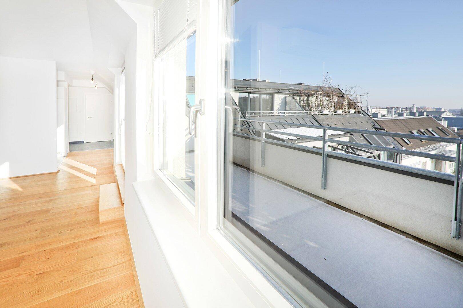 Heller Innenraum mit Blick auf den Balkon und die umliegenden Dächer der Stadt.