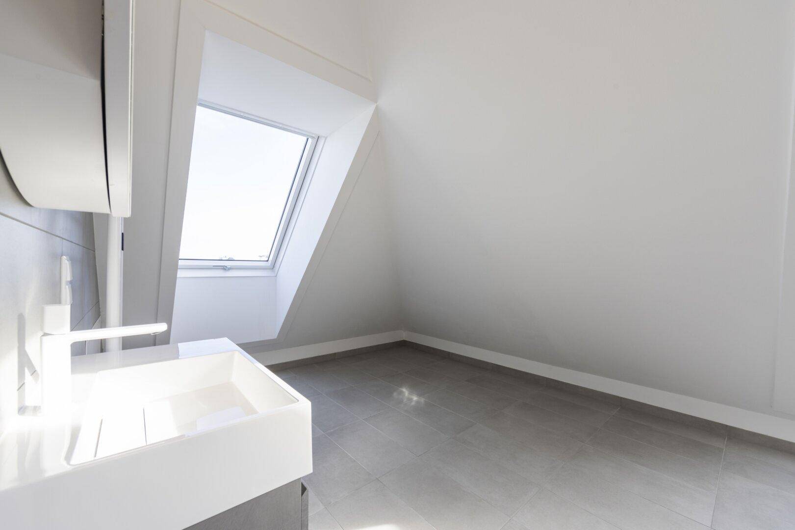 Helles Badezimmer mit grauen Fliesen, modernem Waschbecken und Dachfenster.