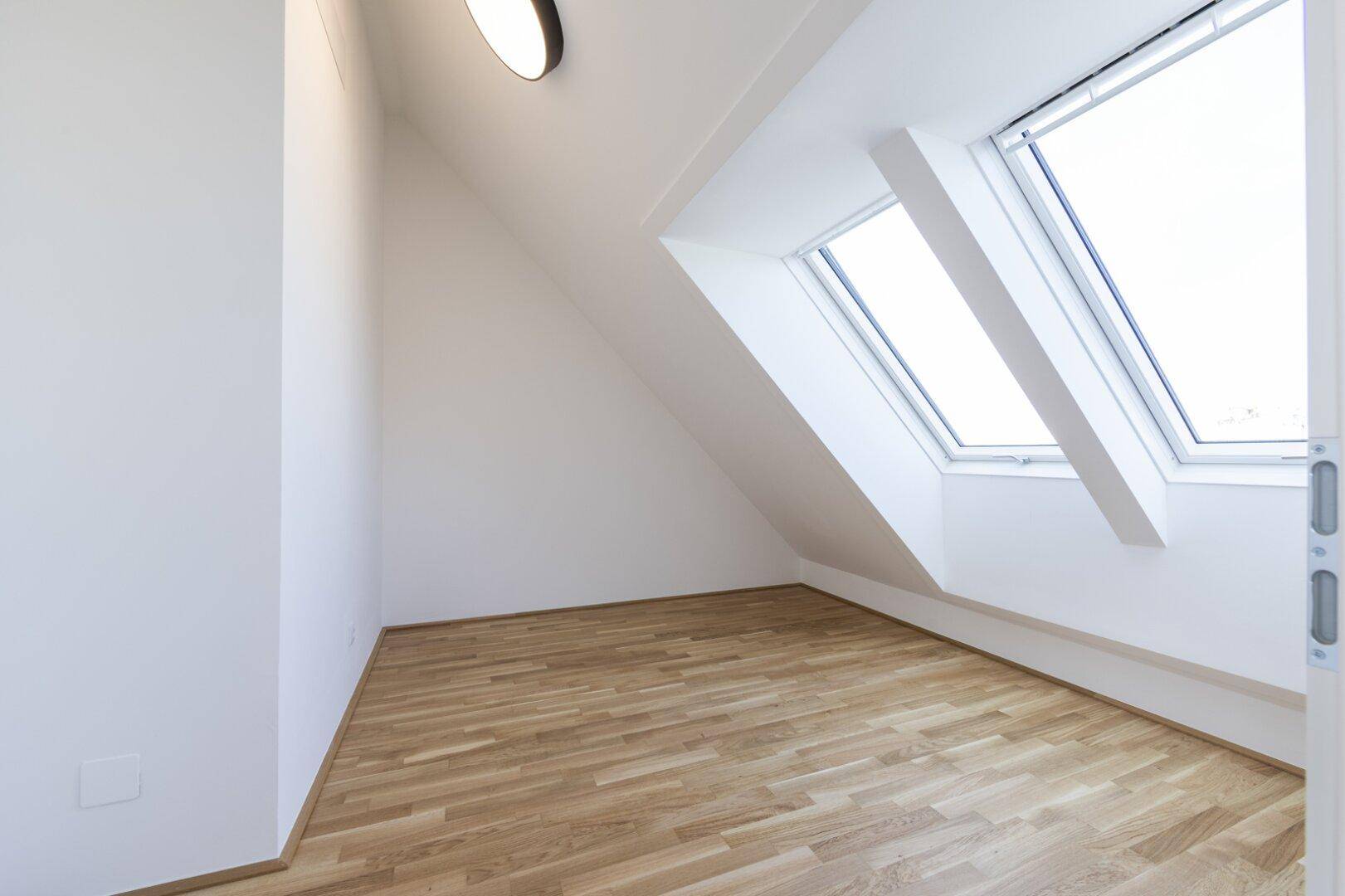 Helles Schlafzimmer im Dachgeschoss mit Parkettboden und zwei Dachfenstern.