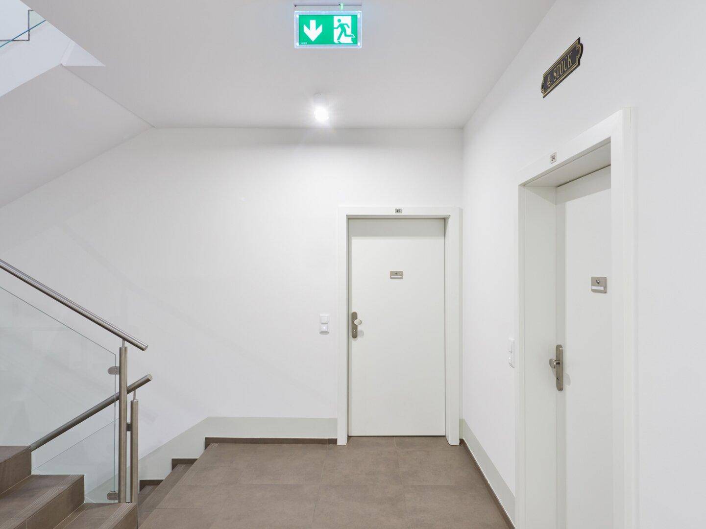 Modernes Treppenhaus mit Glasgeländer, Fliesenboden und klaren Linien.