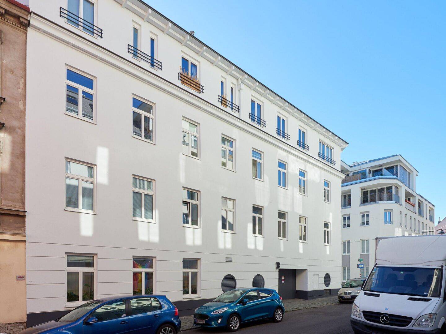Seitenansicht des weißen Gebäudes mit vielen Fenstern und geparkten Autos auf der Straße.
