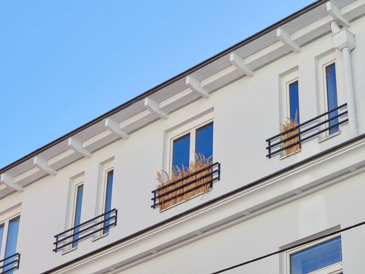 Fenster mit französischen Balkonen, dekoriert mit Trockengräsern, an der weißen Fassade.