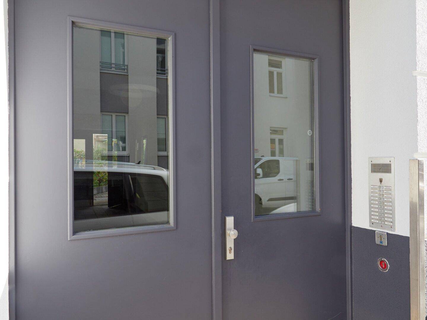 Detailansicht der dunklen Eingangstür mit Glasausschnitten und Gegensprechanlage.