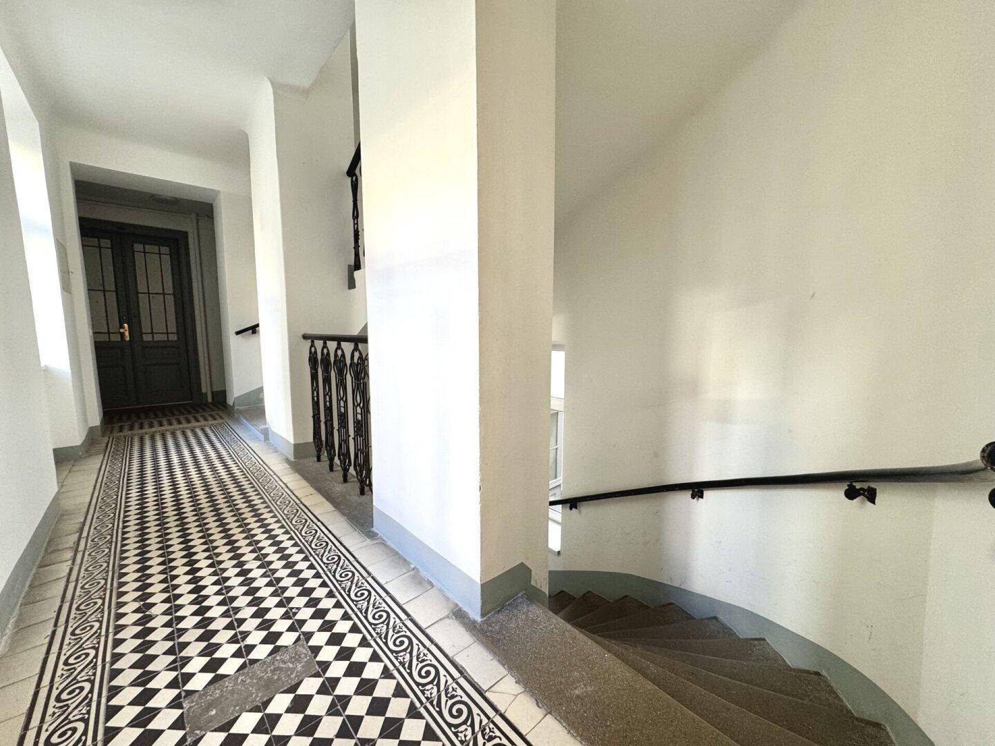 Treppenhaus mit gemustertem Fliesenboden und schmiedeeisernem Geländer in einem Altbau.