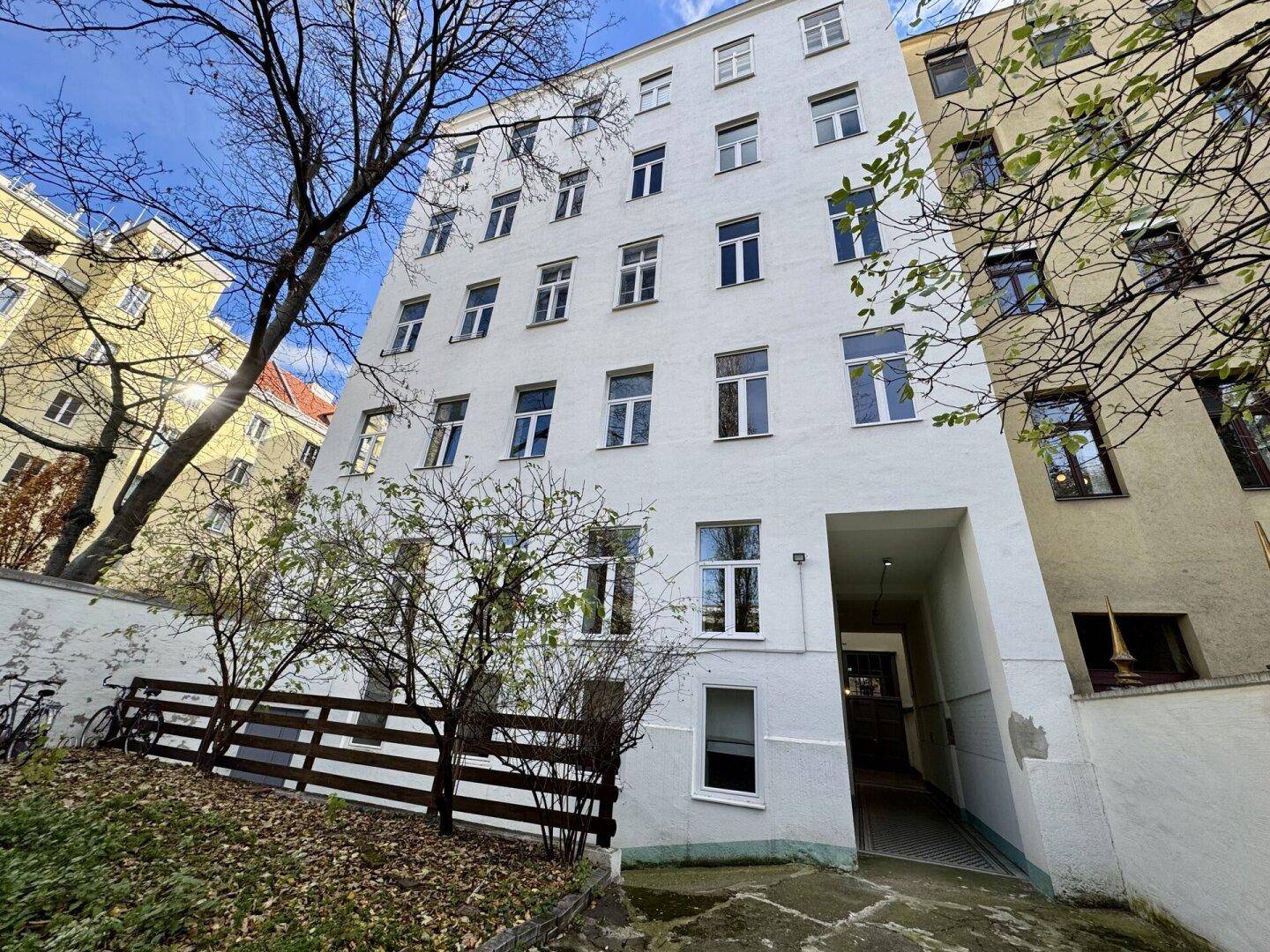 Rückseite eines weißen Wohngebäudes mit mehreren Fenstern und einem Eingangsbereich.