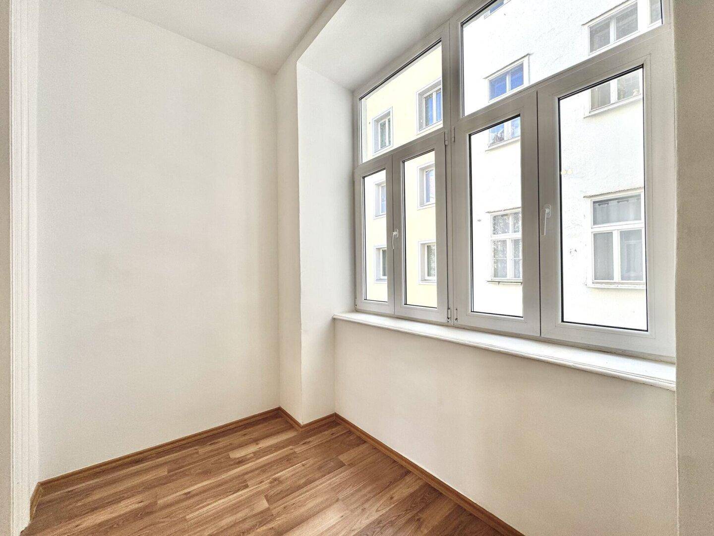 Kleines, helles Zimmer mit Holzboden und großem Fenster mit Blick auf die Umgebung.