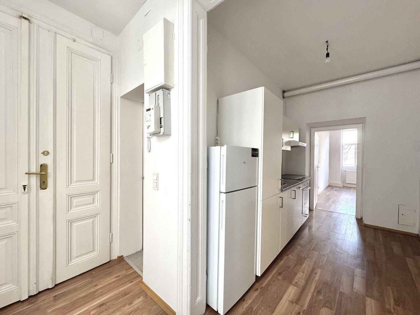 Küchenzeile mit weißen Schränken und Kühlschrank, bereit für die Installation weiterer Geräte.