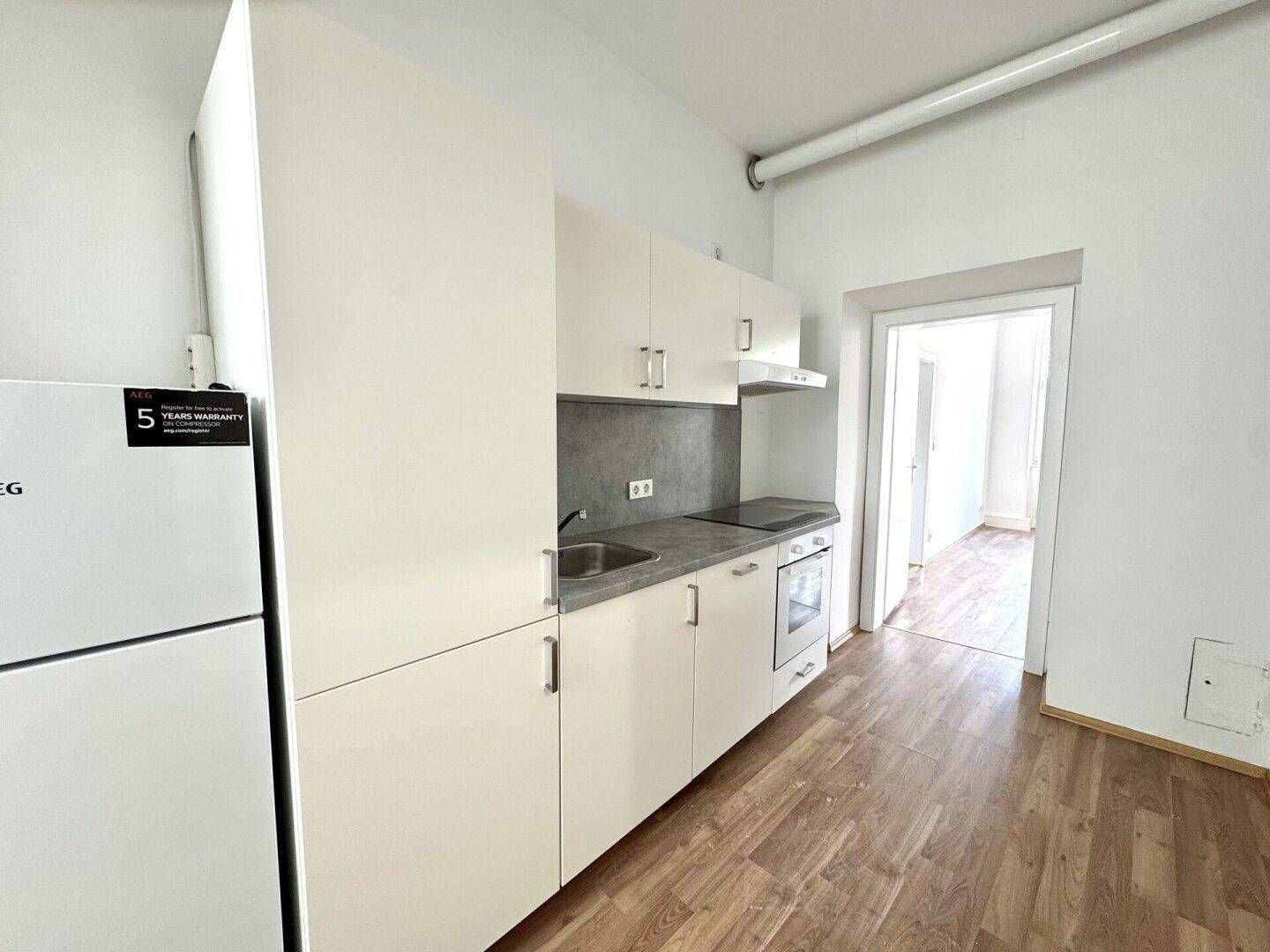 Moderne Küchenzeile mit weißen Schränken, Spüle, Herd und Backofen.