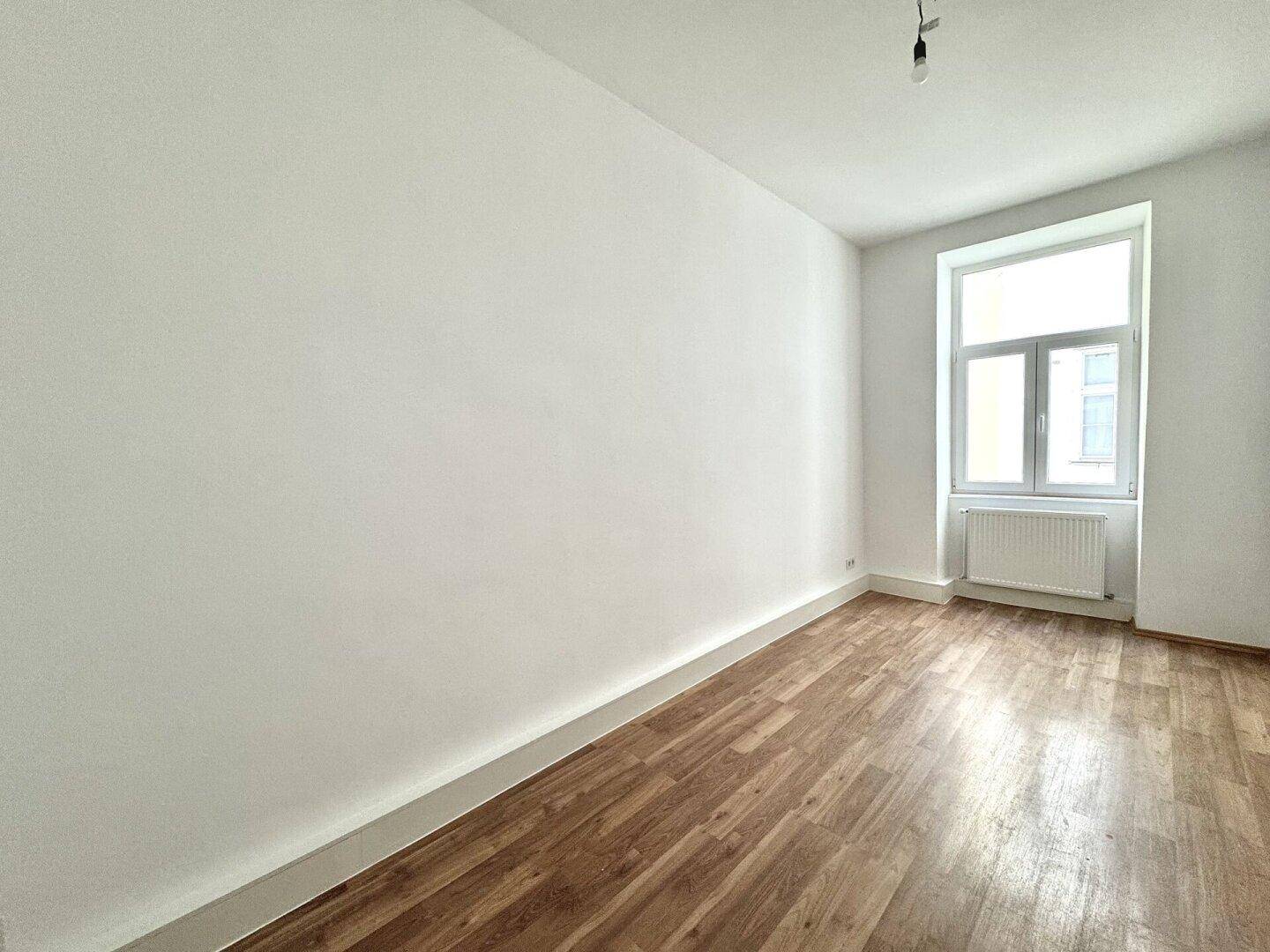 Geräumiges Zimmer mit Holzboden und einem großen Fenster, ideal für Wohn- oder Schlafbereich.
