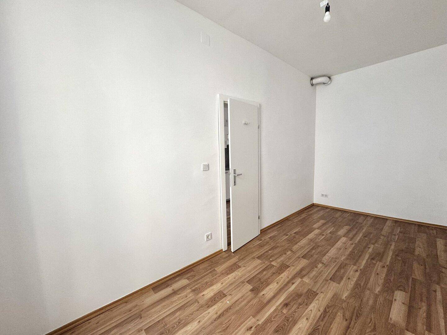 Leeres Zimmer mit Holzboden und weiß gestrichenen Wänden, bietet viel Gestaltungspotenzial.