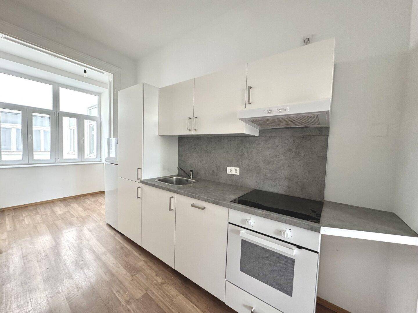 Funktionale Küchenzeile mit weißen Schränken, Herd, Backofen und Blick ins Nebenzimmer.