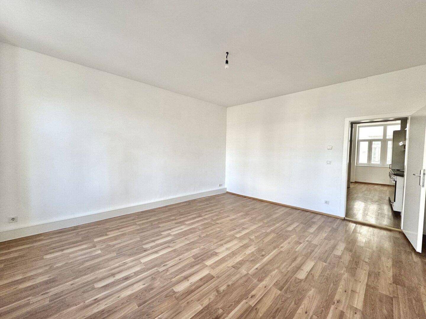 Großes, helles Zimmer mit Holzboden und Zugang zur Küche, ideal für offenes Wohnen.