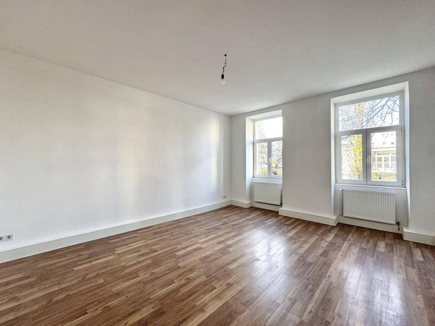 Helles Zimmer mit Holzboden und zwei Fenstern, bietet viel Tageslicht und Ausblick.