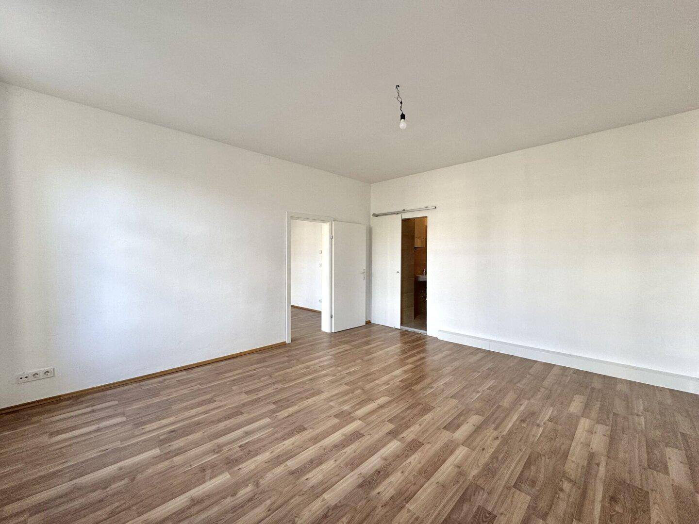 Helles Zimmer mit Holzboden und Schiebetür, die zu einem angrenzenden Bereich führt.
