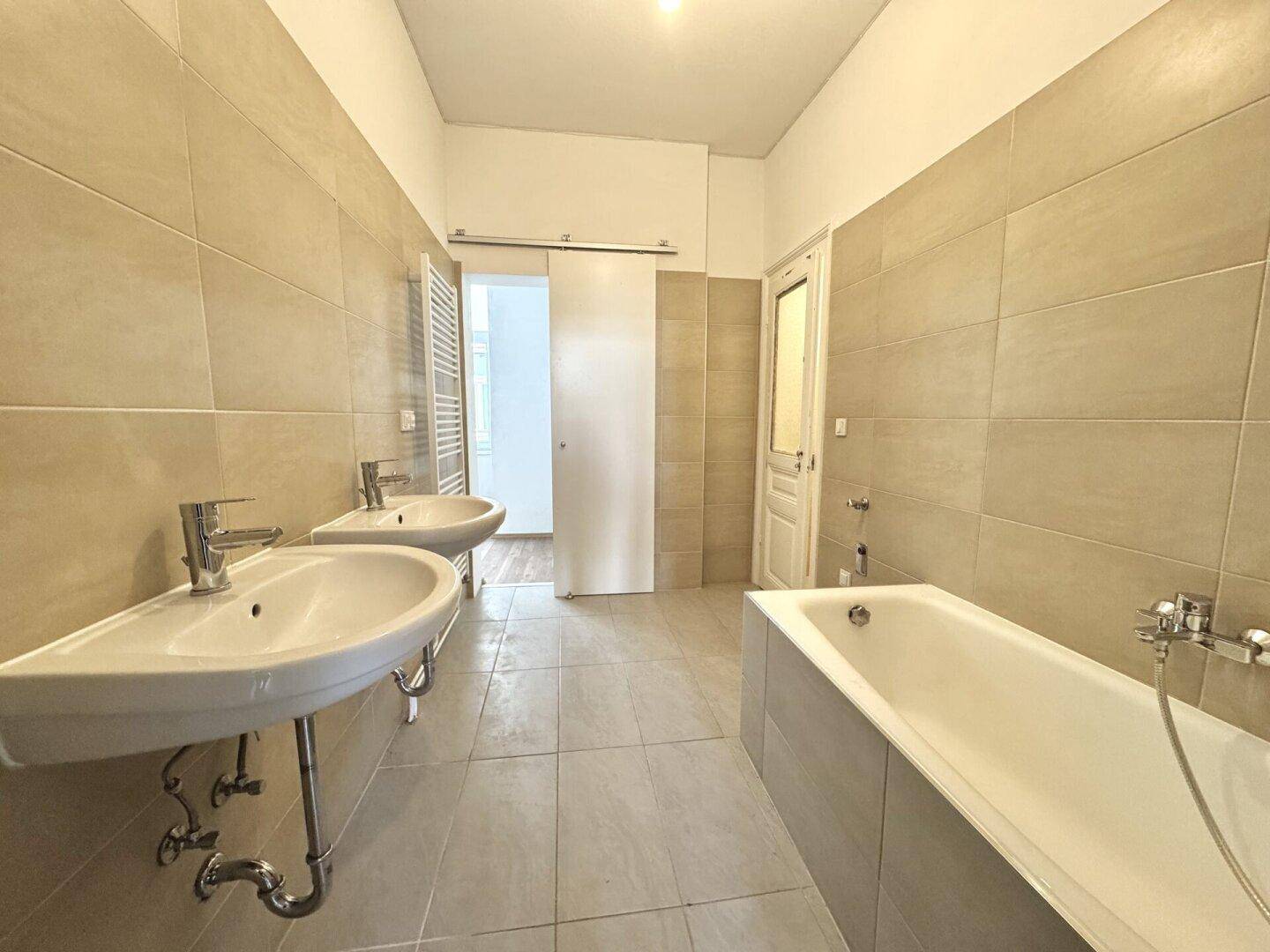 Modernes Badezimmer mit zwei Waschbecken, Badewanne und beigefarbenen Fliesen.